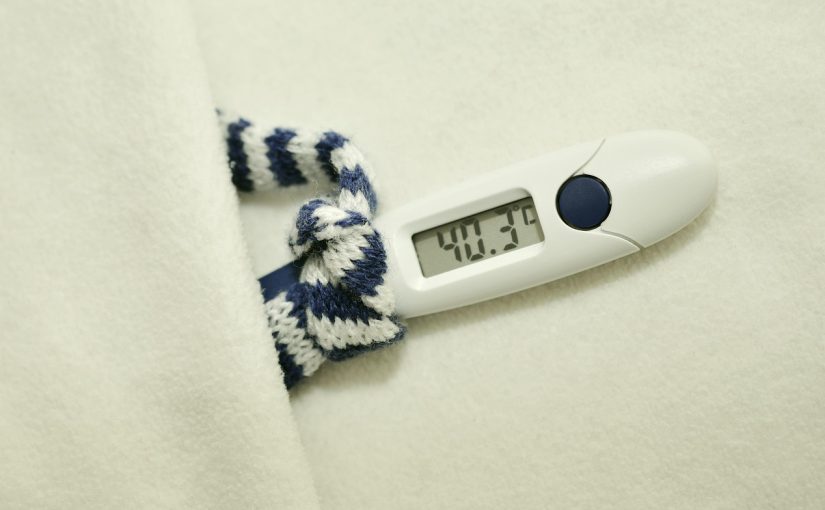 Termometr elektroniczny pokazujący wysoką temperaturę ciała owinięty w koc